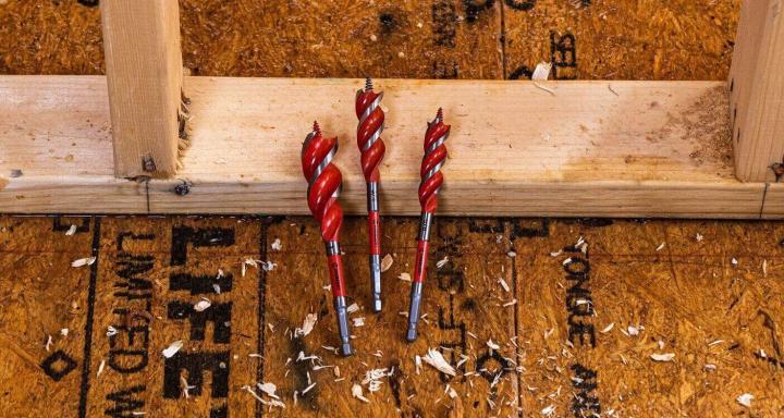 Three Crescent high speed auger wood drill bits laying between a framed wall