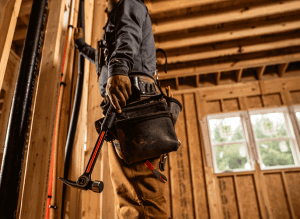 Man standing inside a new construction of a framed house holding a Crescent milled face steel framing hammer